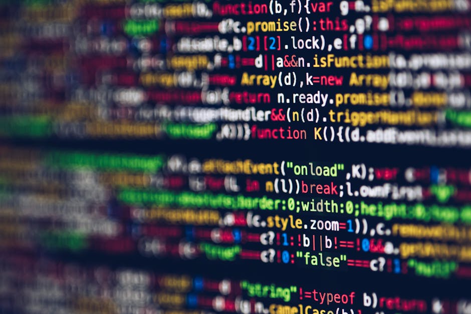 A close-up photograph of a computer screen displaying lines of source code with multicolored syntax highlighting, including keywords, variables, functions, and punctuation, set against a dark backgrou