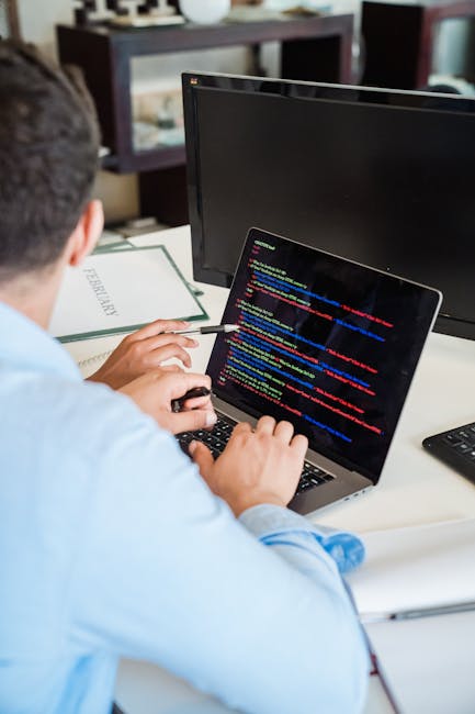 A close-up photograph of a computer screen displaying lines of source code with multicolored syntax highlighting, including keywords, variables, functions, and punctuation, set against a dark backgrou